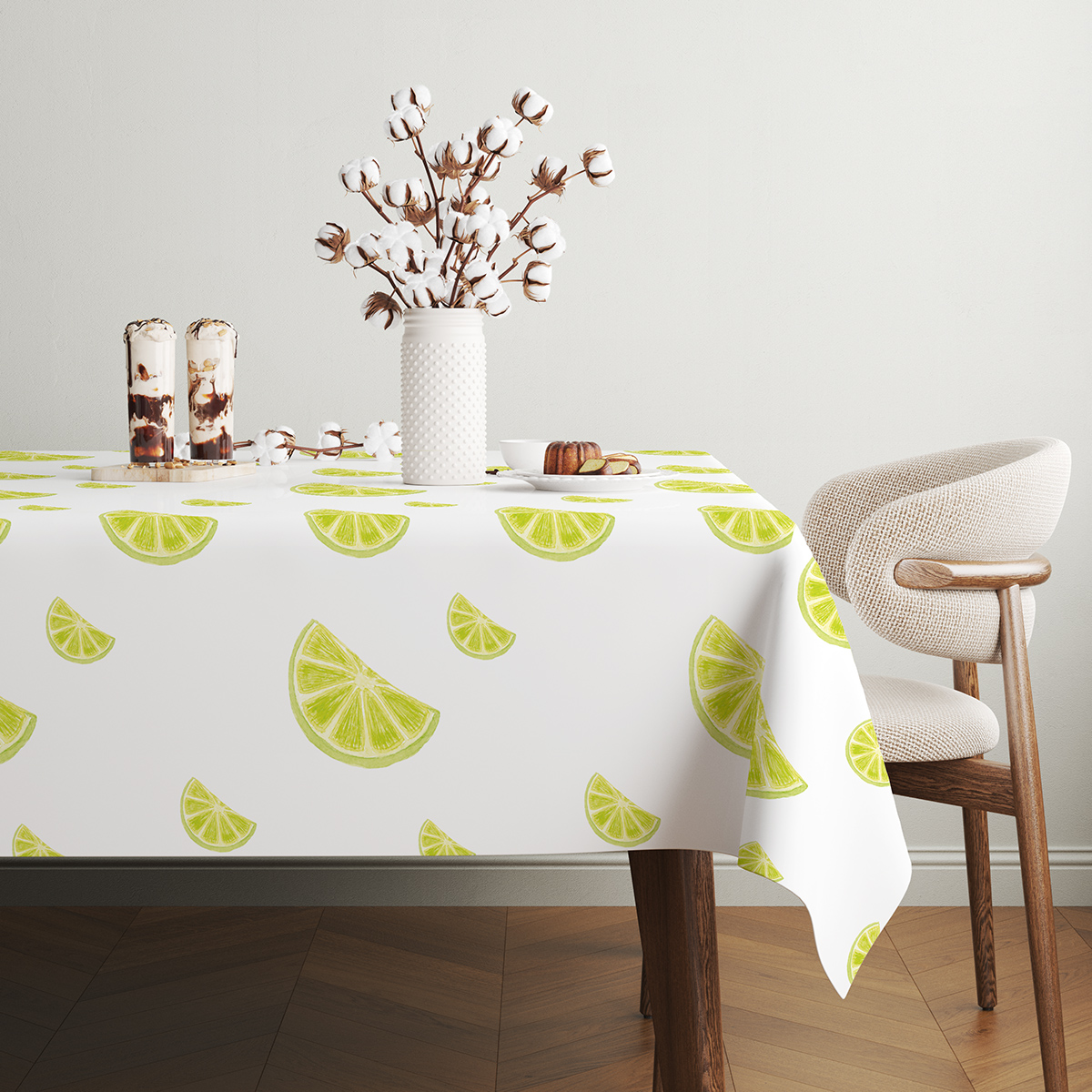 stół nakryty obrusem z limonkowymi plasterkami obok wazonu z bawełnianymi kwiatami i deserów