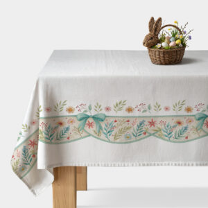 biały obrus z pastelowym kwiatowym brzegiem i miętową kokardą na stole z koszykiem z pisankami