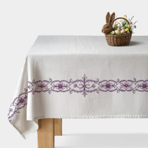biały obrus z fioletowym haftowanym pasem na stole udekorowany koszykiem z pisankami