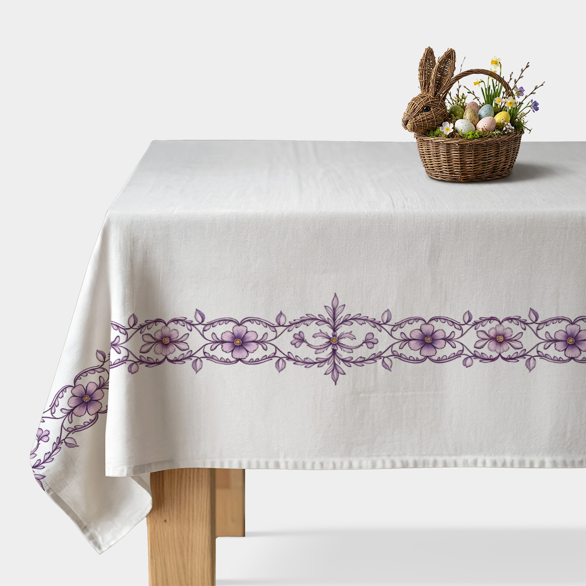 biały obrus z fioletowym haftowanym pasem na stole udekorowany koszykiem z pisankami