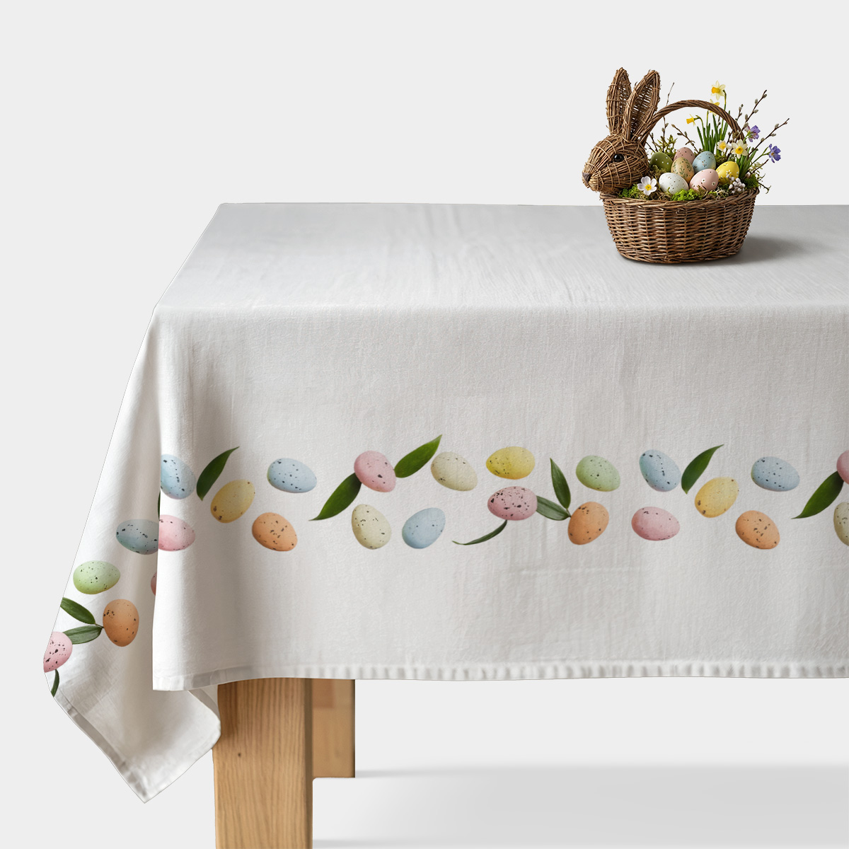 obrus na białym stole z bordiurą pastelowych pisanek i zielonych listków