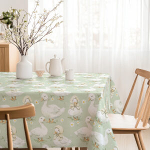 Stół udekorowany obrusm z motywem kaczuszek, filiżanka i wazon z gałązkami