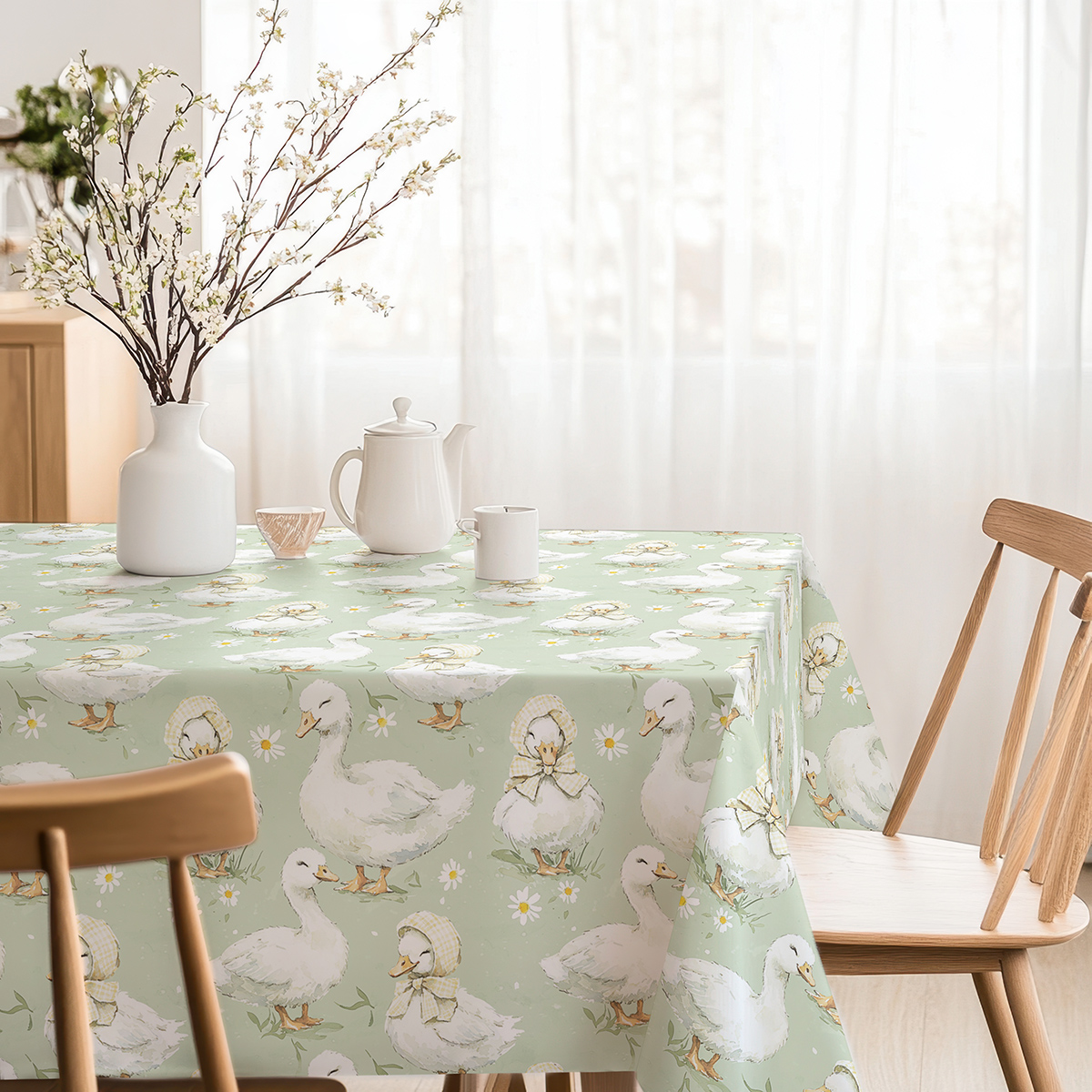 Stół udekorowany obrusm z motywem kaczuszek, filiżanka i wazon z gałązkami