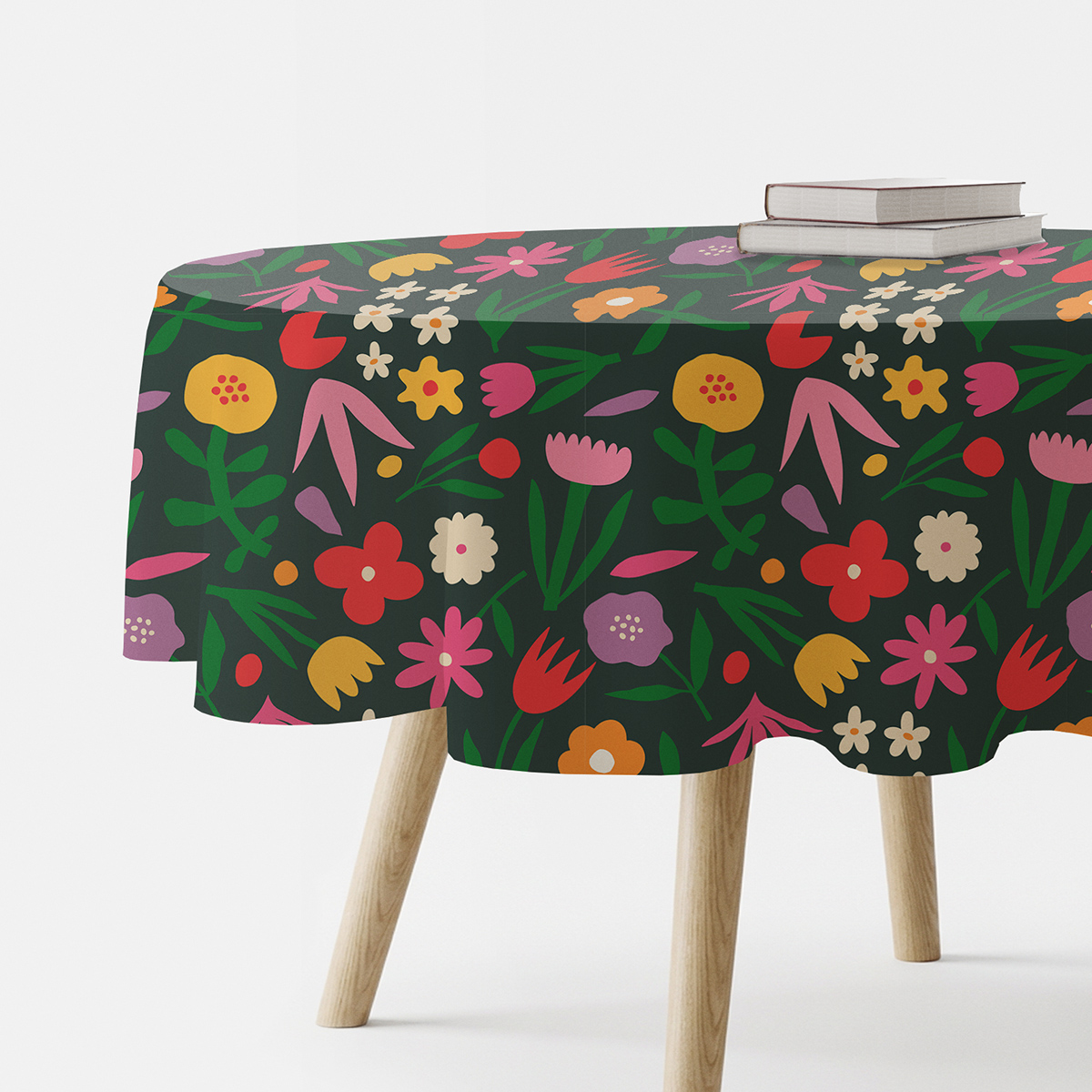Okrągły obrus z żywym wzorem kwiatów na ciemnozielonym tle, widok boczny ze stosem książek