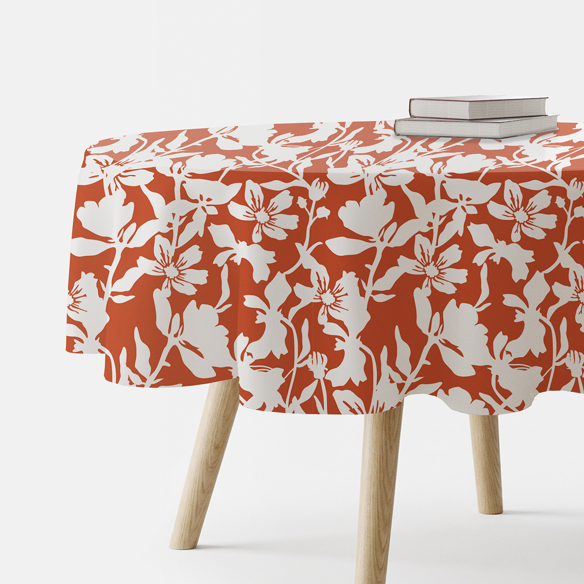 Okrągły obrus z białym wzorem kwiatowym na ceglastym tle na stoliku z książkami