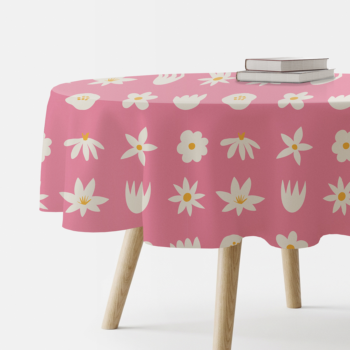 okrągły obrus w różowym tle z białymi stokrotkami na stole z książkami