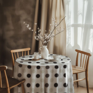 aranżacja stołu z okrągłym obrusem, wazon z gałązkami i filiżanką na tle zasłon