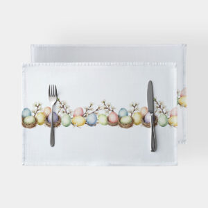 Podkładki obiadowe na białym tle z wzorem pastelowych pisanek i kwitnących gałązek, ustawione ze sztućcami