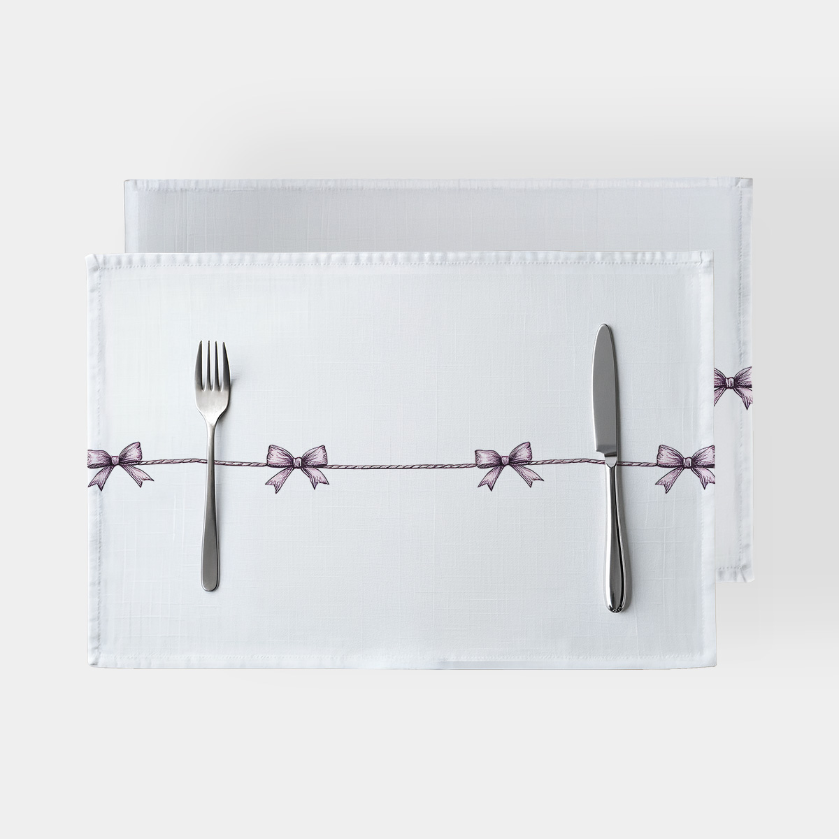 biała podkładka z rzędem drobnych fioletowych kokardek na lince z widocznymi sztućcami