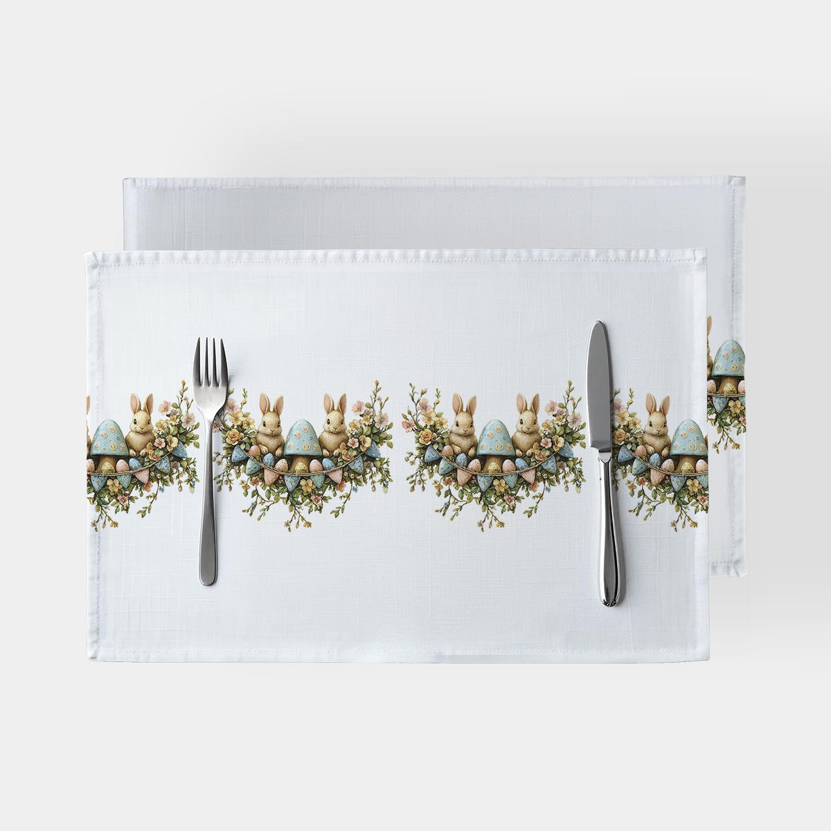 biała podkładka na stół z powtarzającym się motywem zajączka, pisanki i wianuszka widok z góry z sztućcami