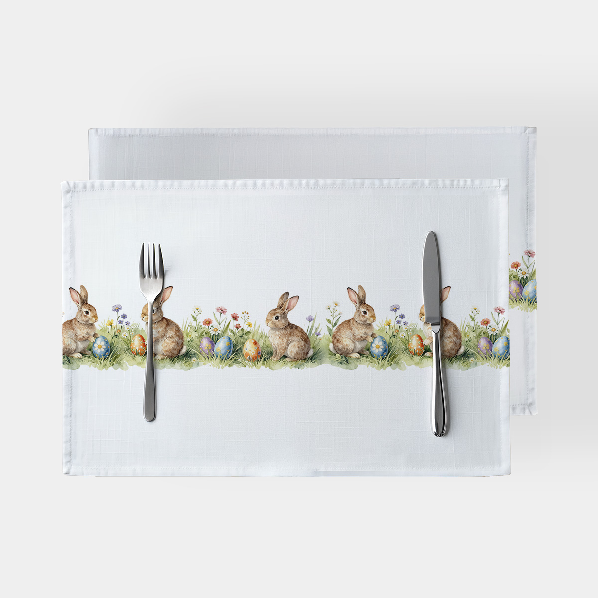 Dwie białe podkładki z nadrukiem zajączków i kolorowych pisanek ułożone jedna na drugiej, widok z góry