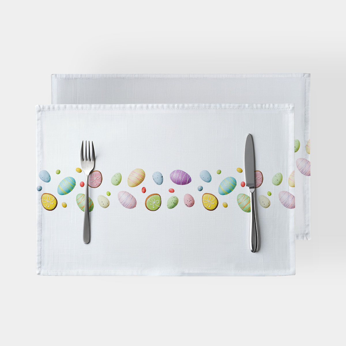 Podkładki stołowe na białym tle z pasem pastelowych pisanek i ciasteczek, ułożone ze sztućcami