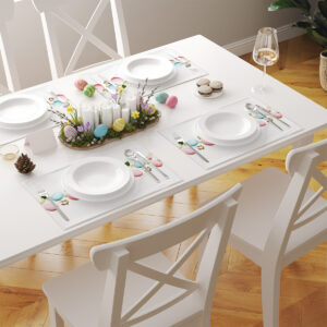 Jasny stół nakryty kilkoma podkładkami z pastelowym motywem pisanek i pąków róż