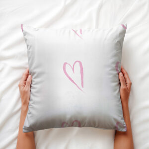 ręce trzymają poduszkę z różowym akwarelowym motywem serca zbliżenie na wzór