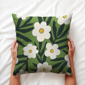 Dłoń trzymająca poduszkę z motywem białych kwiatów na zielonym tle, ujęcie na łóżku