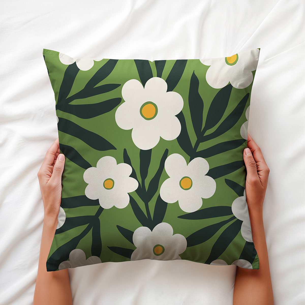 Dłoń trzymająca poduszkę z motywem białych kwiatów na zielonym tle, ujęcie na łóżku
