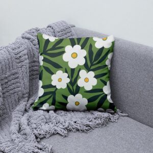 Poduszka z białymi kwiatami na zielonym tle ułożona na szarej sofie obok pledu