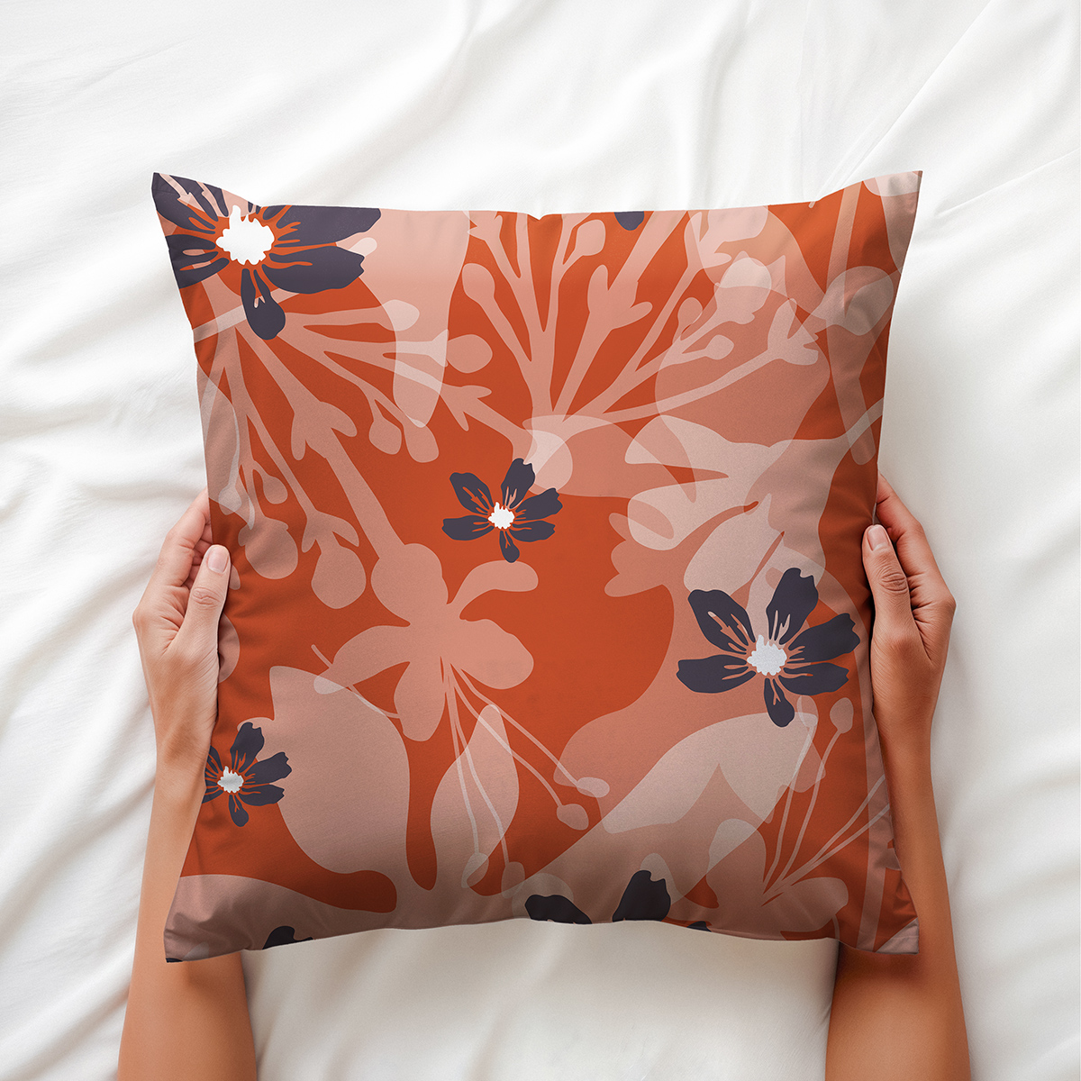 Ręce trzymające poduszkę z motywem kwiatowym na białej pościeli, widoczne detale wzoru