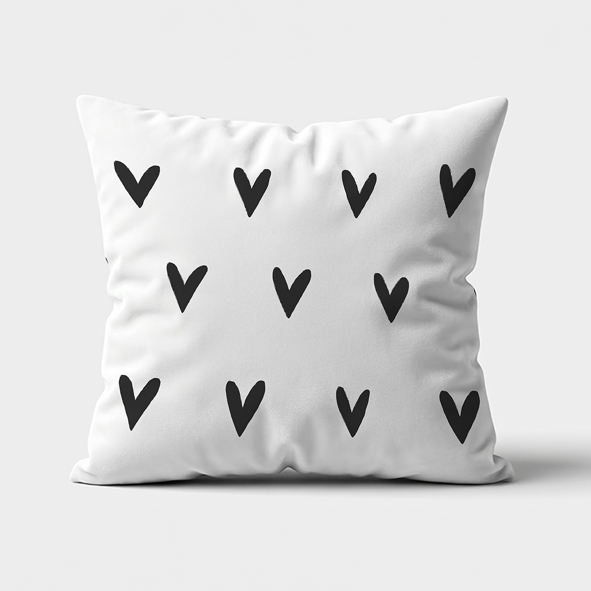 Biała poduszka dekoracyjna z czarnym wzorem serduszek, ujęcie z przodu na jasnym tle