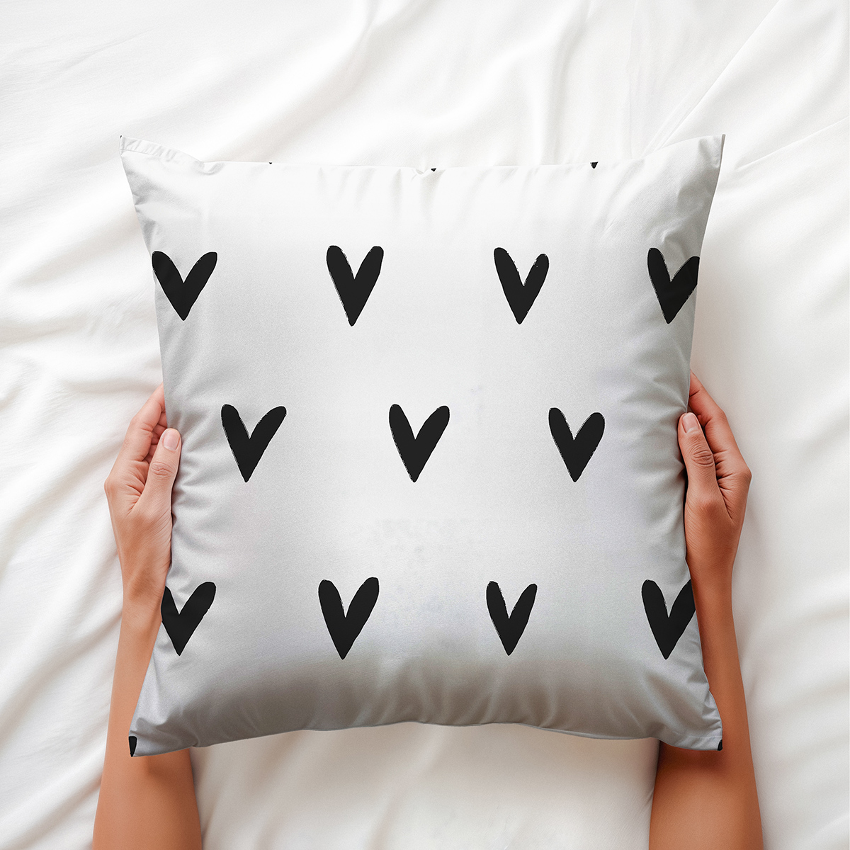Ręce trzymające poduszkę z czarnymi serduszkami, widok aranżacyjny na pościeli