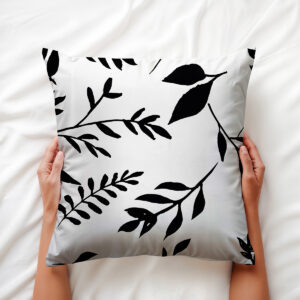 Zbliżenie aranżacyjne poduszki trzymanej w dłoniach, widoczny graficzny motyw liści