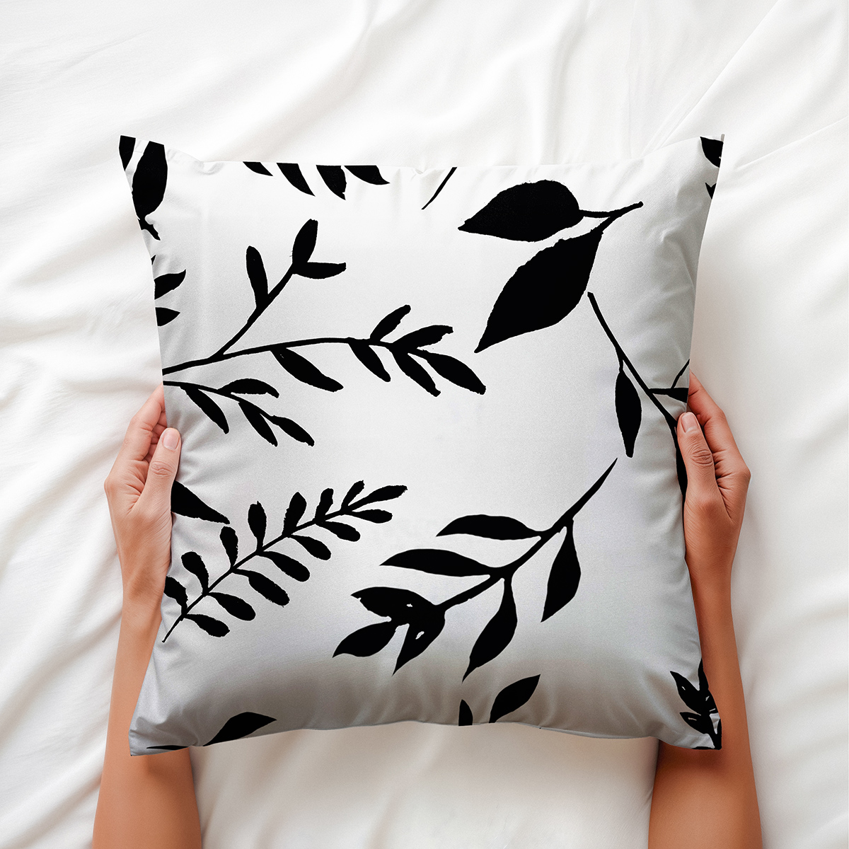 Zbliżenie aranżacyjne poduszki trzymanej w dłoniach, widoczny graficzny motyw liści