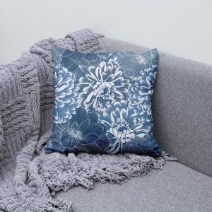 Poduszka dekoracyjna z motywem chryzantem ułożona na szarej kanapie obok pleda