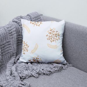 Poduszka dekoracyjna ułożona na szarej kanapie obok pledu, detal wzoru gałązek