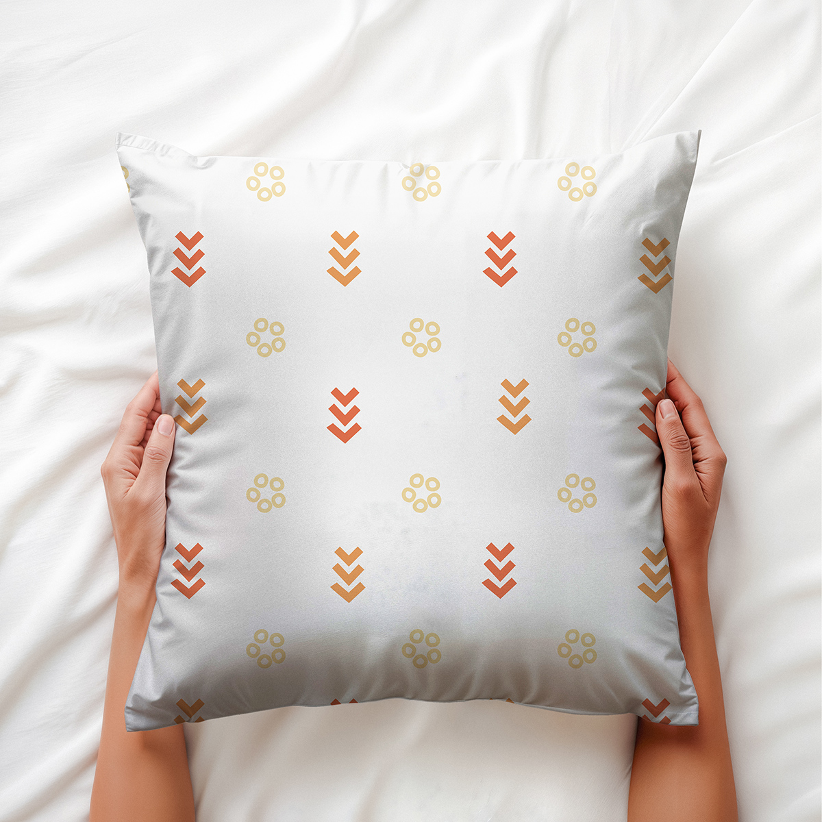 Poduszka trzymana w dłoniach na jasnej pościeli, widoczny powtarzalny motyw kółek i schodkowych strzałek
