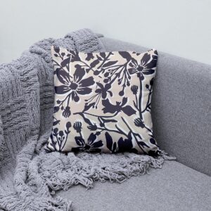 Poduszka ustawiona na szarej sofie obok pledu, detal motywu kwiatowego i neutralne tony