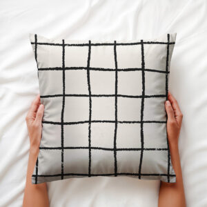 Widok poduszki trzymanej w dłoniach na białej pościeli ukazujący detal wzoru