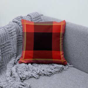 Aranżacja na kanapie z poduszką w czerwono-czarnej kracie obok pledu