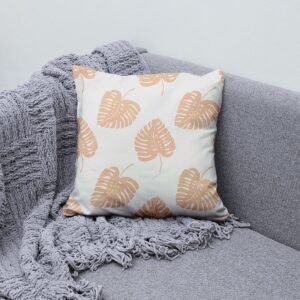 Poduszka ozdobna z liściastym wzorem ułożona na kanapie obok pledu
