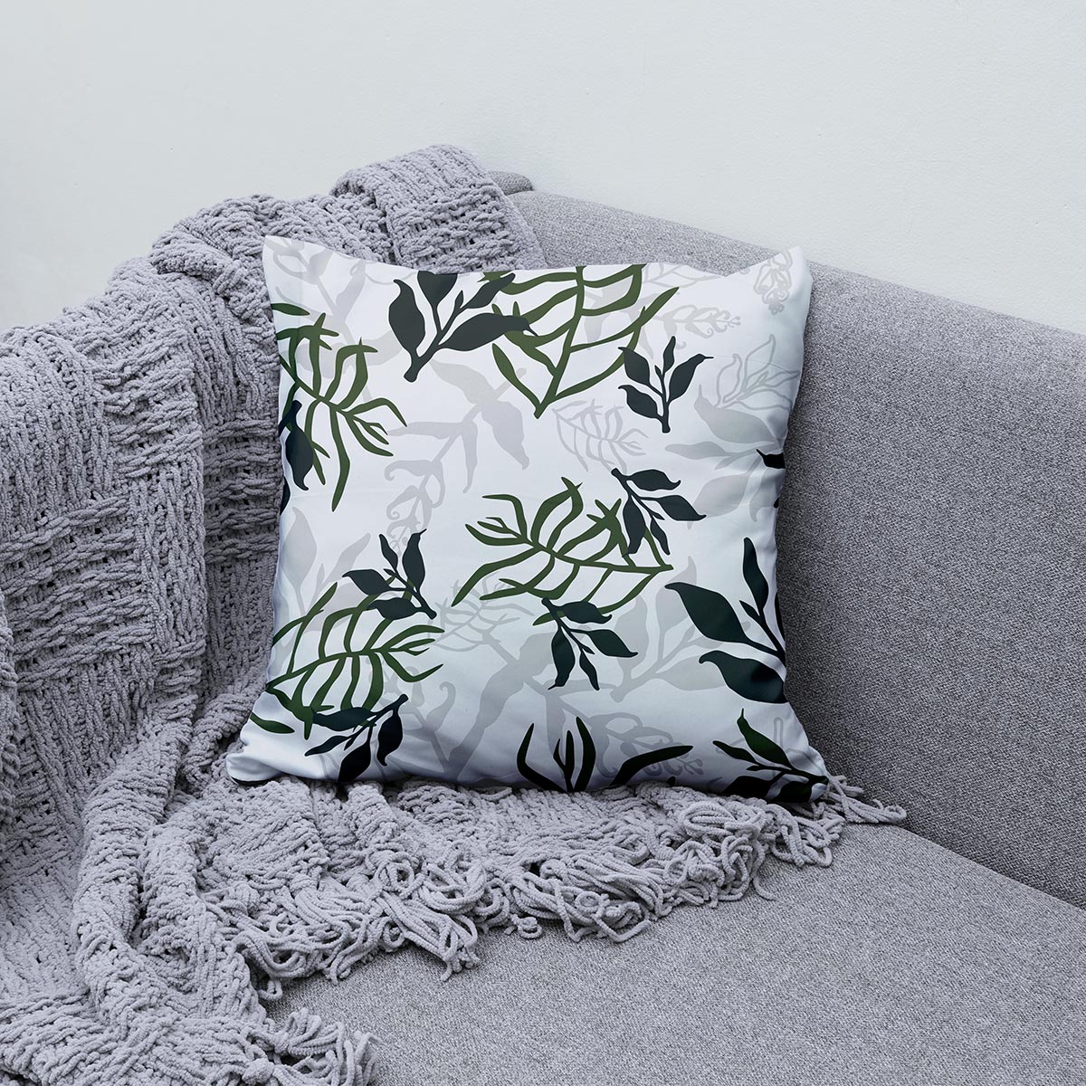 Poduszka z liściastym wzorem na szarej sofie obok pledu
