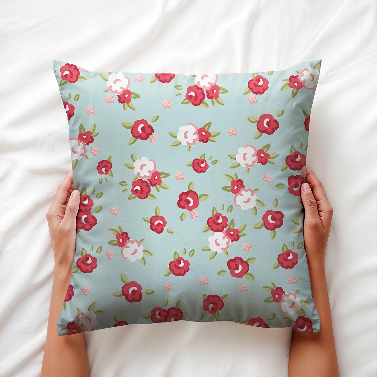 Ręce trzymające poduszkę na białej pościeli, zbliżenie na wzór drobnych różyczek