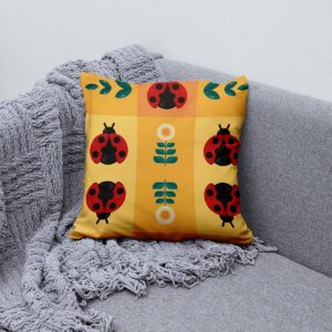 Poduszka z wzorem biedronek ułożona na kanapie obok miękkiego pleda