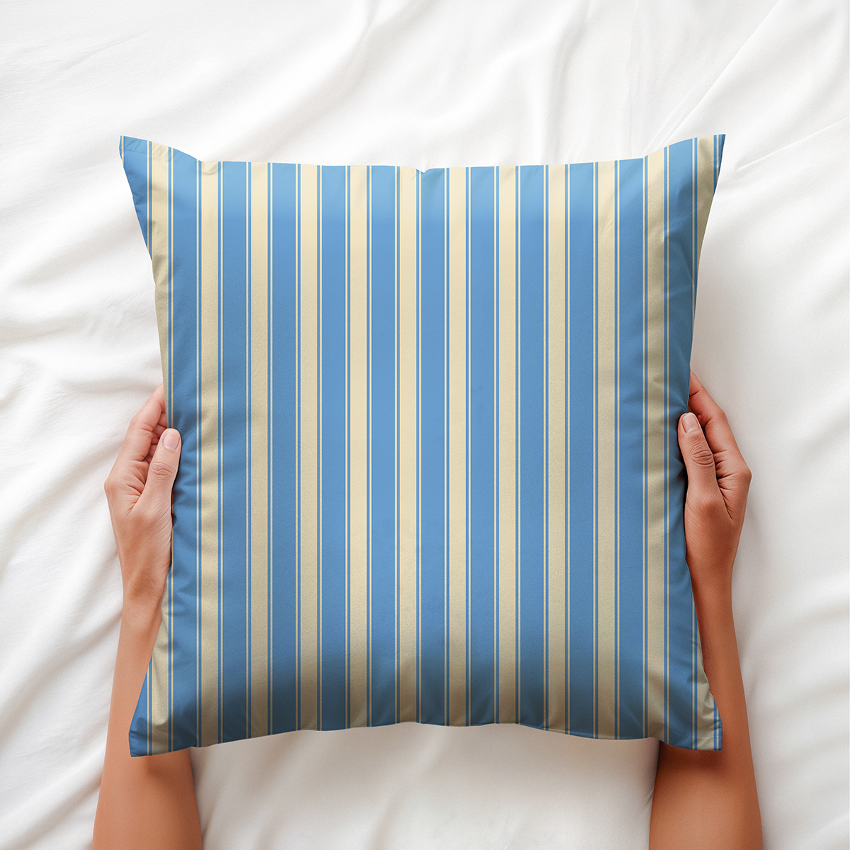 Ręce trzymające poduszkę z jasnoniebieskimi i kremowymi paskami nad białą pościelą