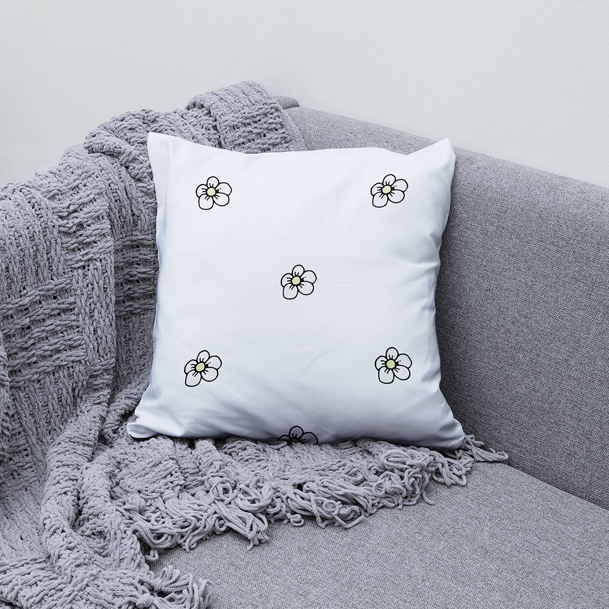 Poduszka ułożona na kanapie obok pledu, detal kwiatuszków z czarną konturą i żółtym środkiem