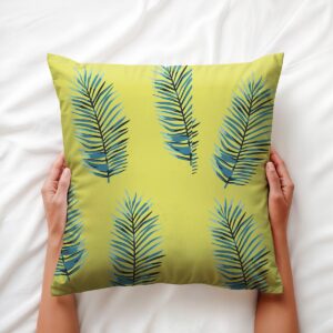 Ręce trzymające poduszkę z tropikalnym motywem liści palmowych na jasnej pościeli