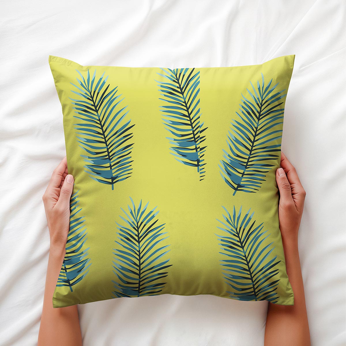 Ręce trzymające poduszkę z tropikalnym motywem liści palmowych na jasnej pościeli