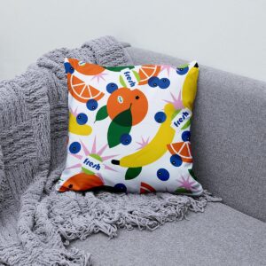 Poduszka dekoracyjna ułożona na kanapie obok pleda jako aranżacyjny akcent z motywem owoców