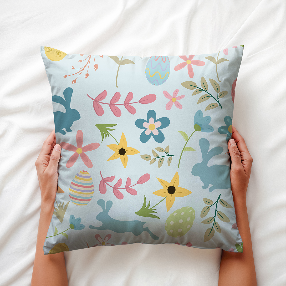 Poduszka trzymana w dłoniach na białej pościeli, widoczne pastelowe zajączki i pisanki