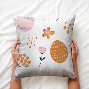 Dłoń trzymająca poduszkę z pastelowymi pisankami i drobnymi kwiatkami — aranżacja trzymana w dłoniach