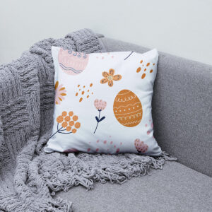 Poduszka z motywem pisanek ułożona na kanapie obok szarego koca — ujęcie aranżacyjne