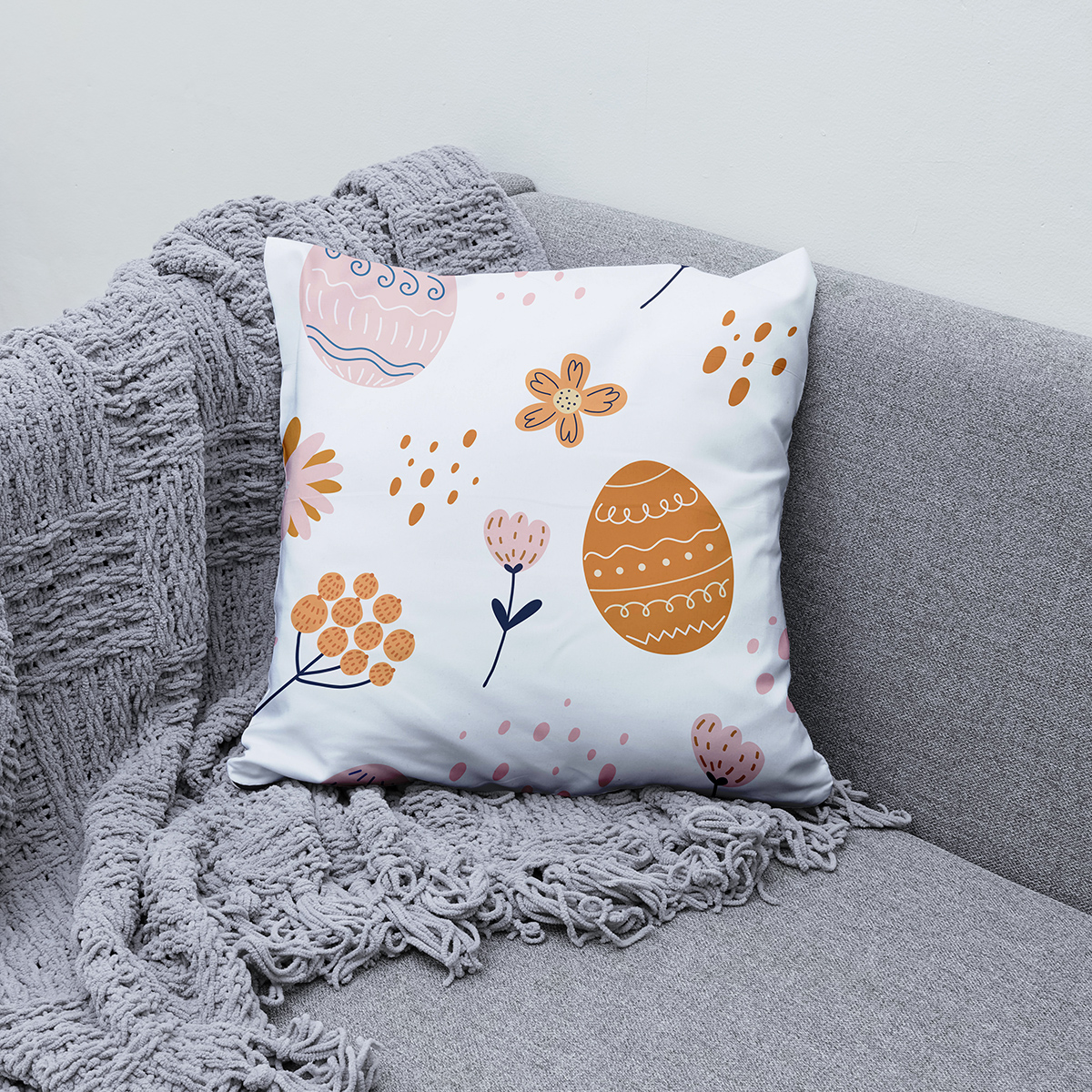 Poduszka z motywem pisanek ułożona na kanapie obok szarego koca — ujęcie aranżacyjne
