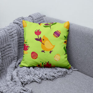 Poduszka ułożona na szarej sofie obok pledu, widoczny cały wzór z kurczakiem i pisankami