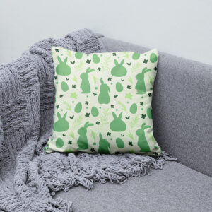 Poduszka z zielonym wzorem zajączków ułożona na kanapie obok pledu