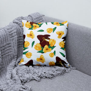 Poduszka z wzorem zająca i żółtych tulipanów ułożona na kanapie przy szarym kocu