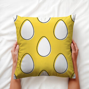 Widok z góry, osoba trzyma poduszkę obiema dłońmi na jasnej pościeli, widoczny wzór pisanek