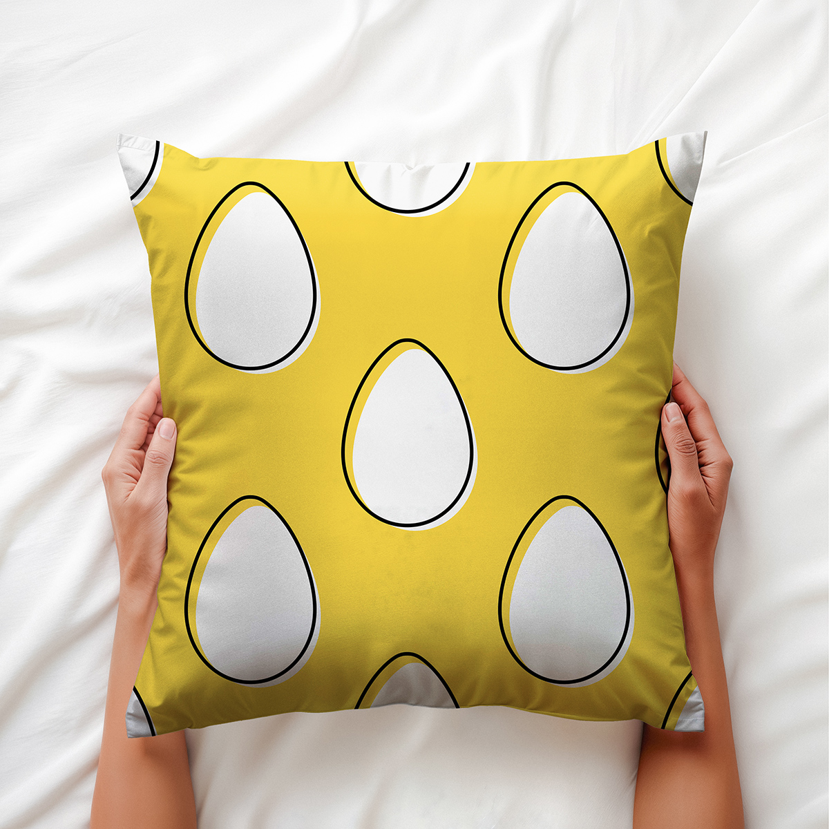 Widok z góry, osoba trzyma poduszkę obiema dłońmi na jasnej pościeli, widoczny wzór pisanek